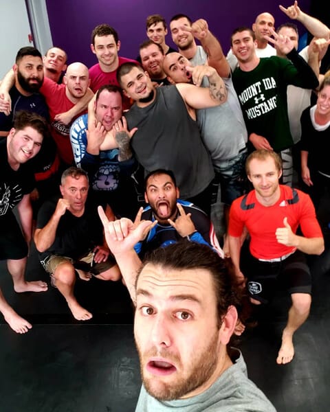 A big group of smiling adult students crowded together after class at Dark Side Jiu-Jitsu