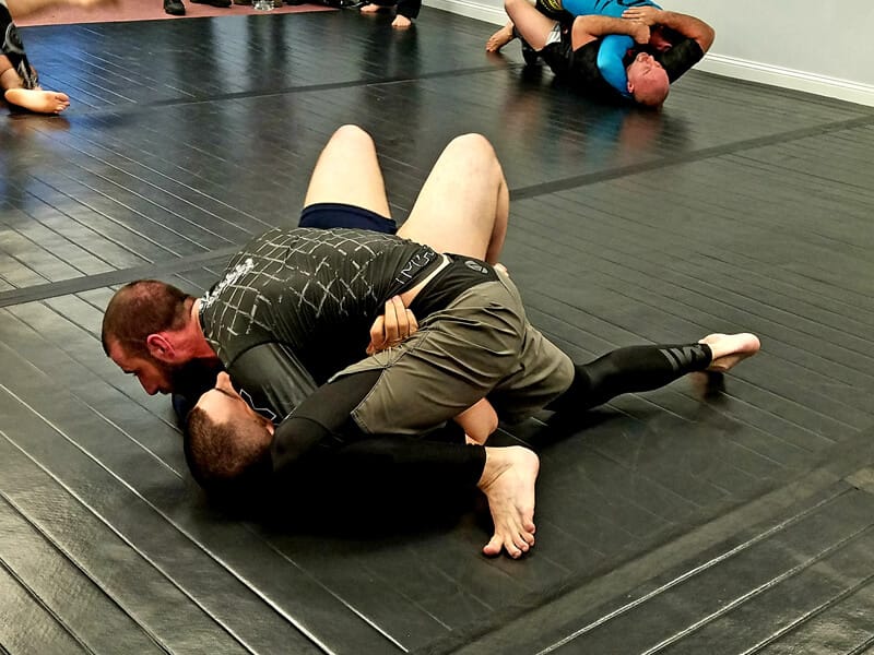Two adult students drilling no-gi jiu-jitsu on the mats at Dark Side Jiu-Jitsu in Plainville