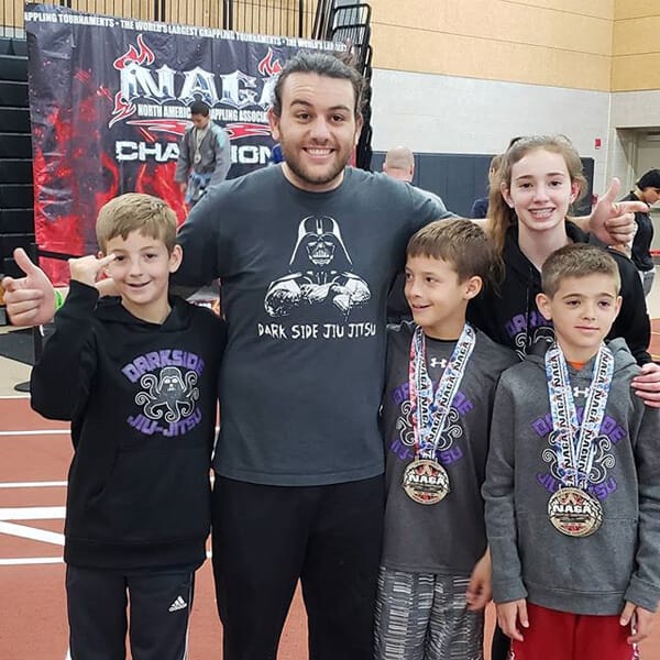 Dark Side kids team with medals at a grappling tournament, coach in the middle